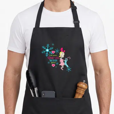 Funny cindy lou who apron - Cindy-Lou Who holding striped stocking next to I've been Cindy-Lou WHO good text — shown on a black cotton canvas apron against a white background
