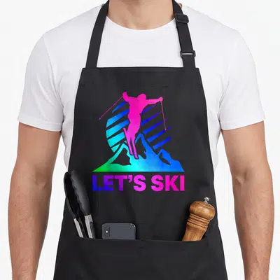 Ski 80s apron - Pink skier silhouette over blue mountains with striped sun and LET'S SKI text — shown on a black cotton canvas apron against a white background