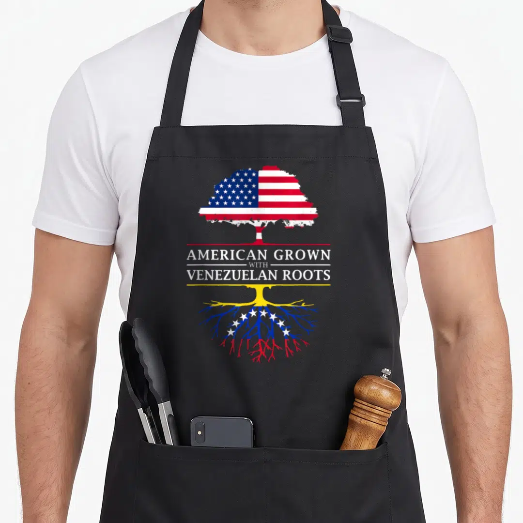 Grown venezuela apron - Tree graphic split by text with US stars stripes and Venezuelan roots in red white blue yellow — shown on a black cotton canvas apron against a white background