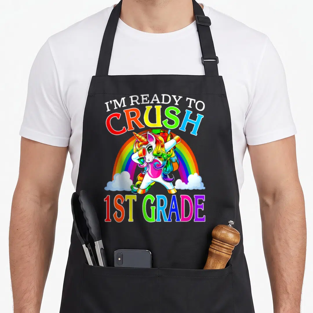 Ready crush unicorn apron - Rainbow cartoon unicorn dabbing with backpack containing apple and pencil under split text — shown on a black cotton canvas apron against a white background