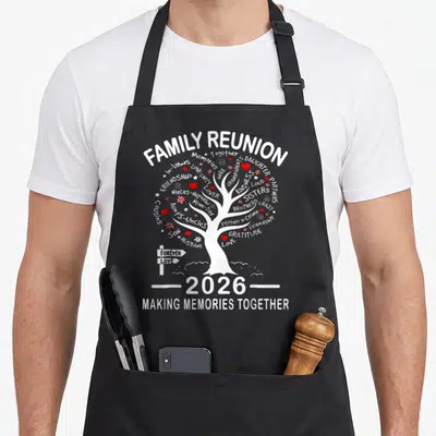 Making family memory apron - White family tree with red hearts and words like Daughter Partners Love Unity 2026 Making — shown on a black cotton canvas apron against a white background
