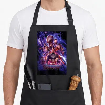 Studio space apron - Avengers Endgame character collage with Captain America and stacked logo text — shown on a black cotton canvas apron against a white background