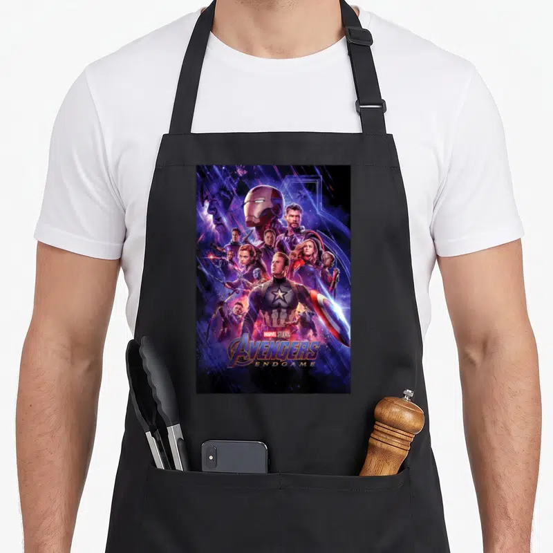 Studio space apron - Avengers Endgame character collage with Captain America and stacked logo text — shown on a black cotton canvas apron against a white background