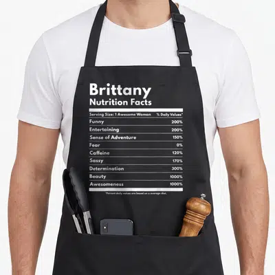 Nutrition brittany apron - White typography listing Brittany Nutrition Facts with percentages for funny, sassy — shown on a black cotton canvas apron against a white background
