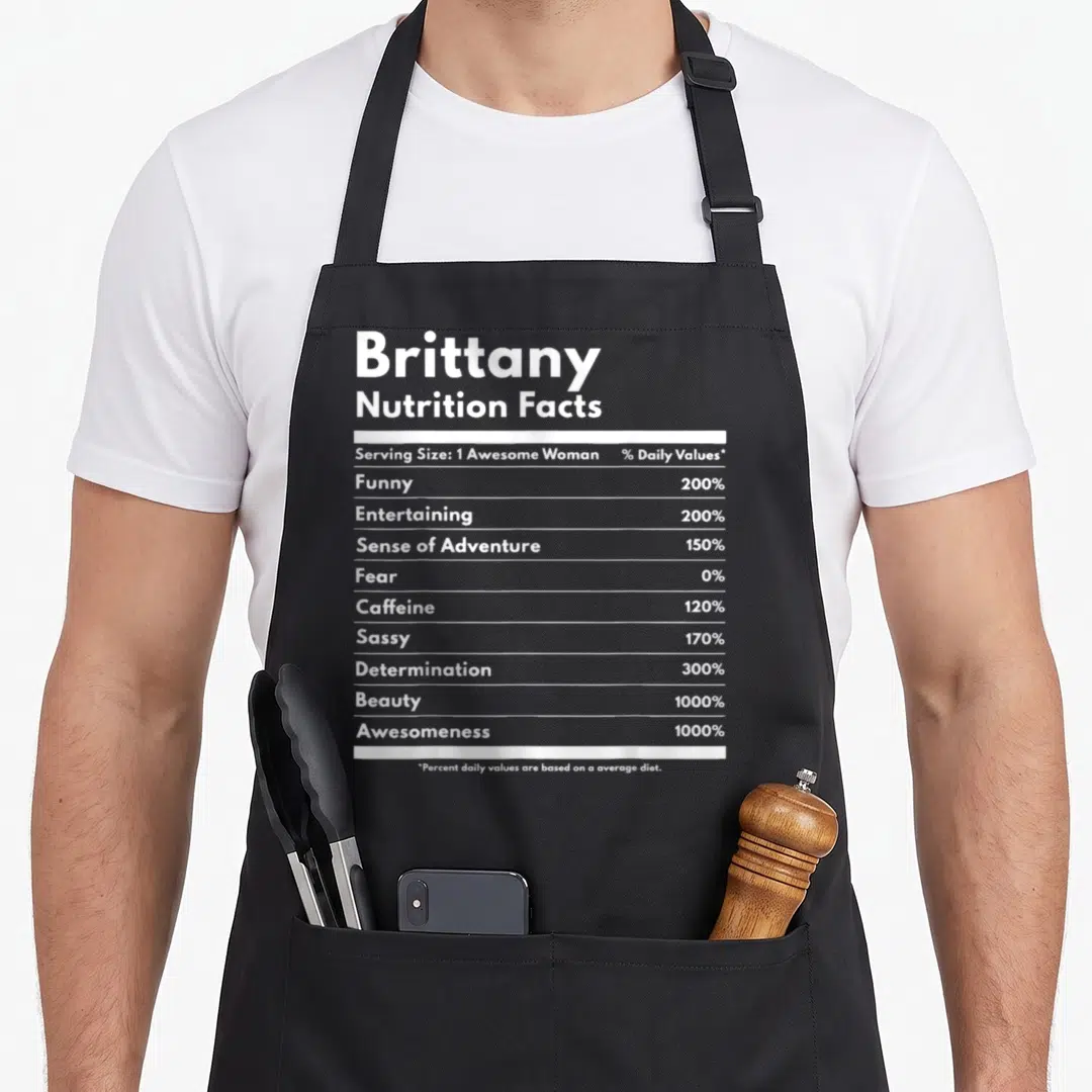 Nutrition brittany apron - White typography listing Brittany Nutrition Facts with percentages for funny, sassy — shown on a black cotton canvas apron against a white background
