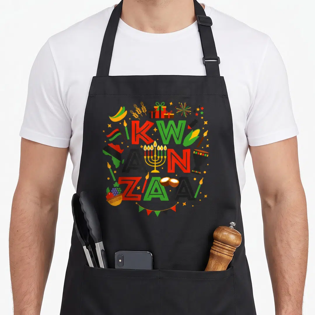 Funny kwanzaa apron - Stacked KWA ANZA ZAA text with corn, drum, flag, and bunting in red green black yellow cartoon — shown on a black cotton canvas apron against a white background