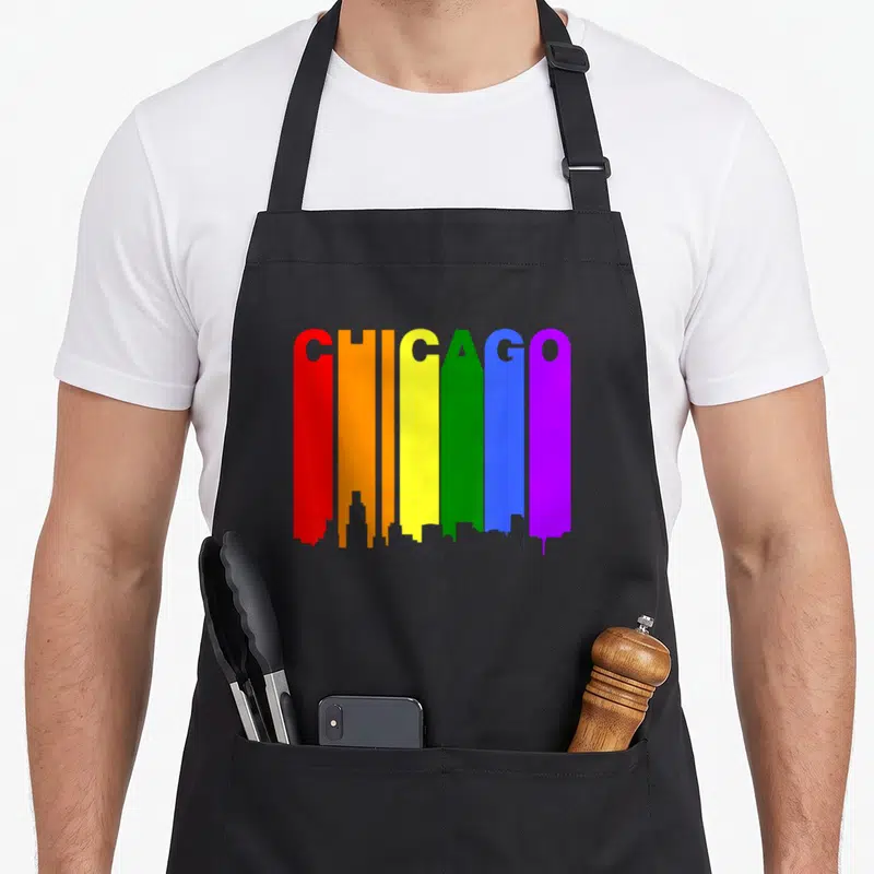 Chicago gay pride apron - CHICAGO in rainbow letters forming skyline silhouette with red orange yellow green blue purple — shown on a black cotton canvas apron against a white background