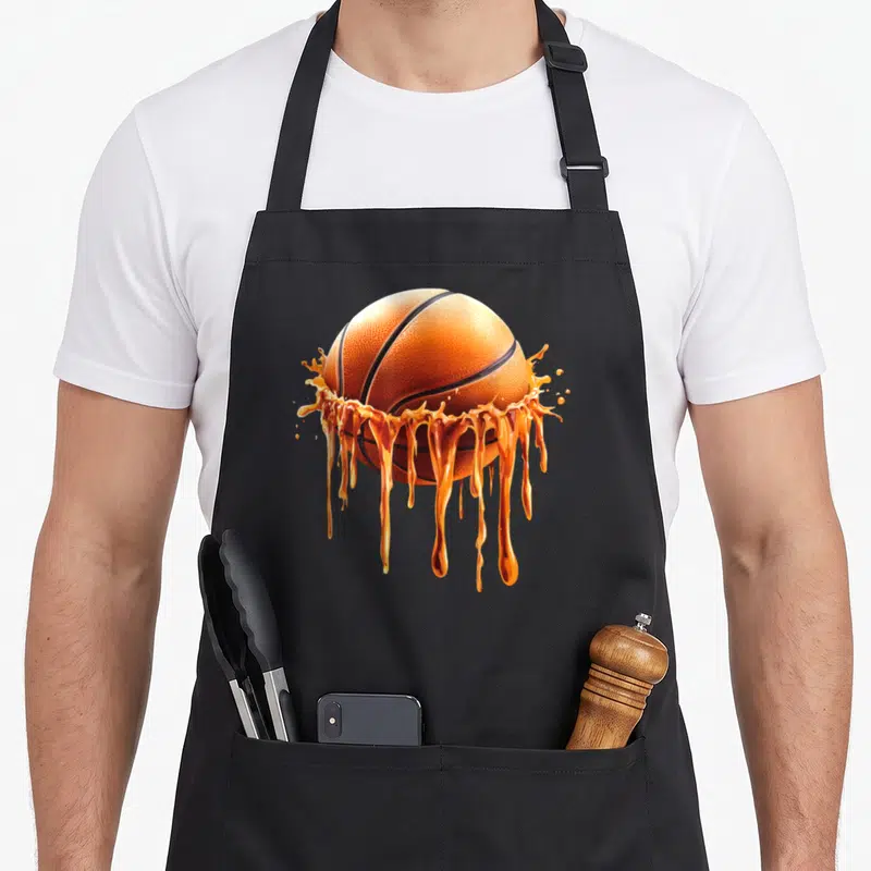 Funny basketball drip apron - Realistic orange basketball surrounded by splashing liquid drips and black lines — shown on a black cotton canvas apron against a white background