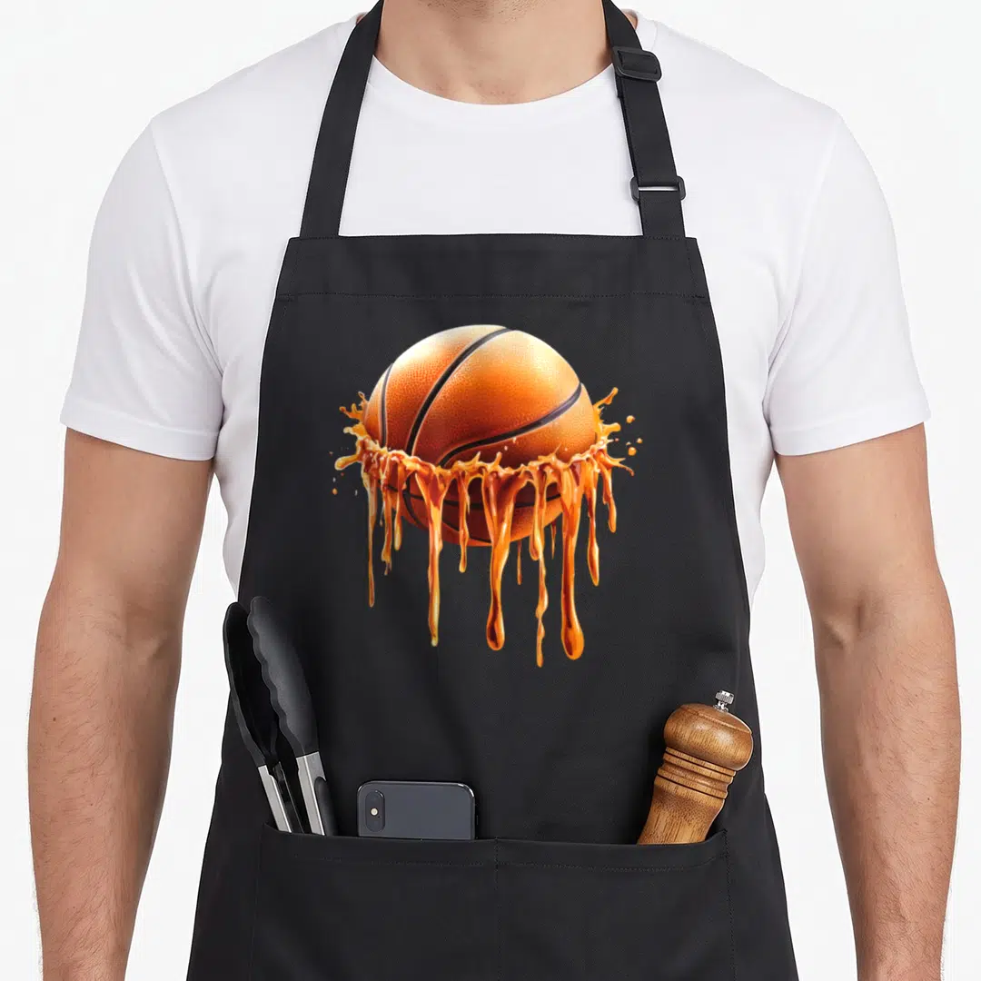 Funny basketball drip apron - Realistic orange basketball surrounded by splashing liquid drips and black lines — shown on a black cotton canvas apron against a white background