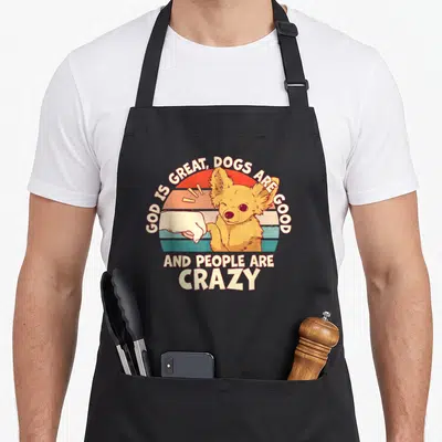 God cooking with dog apron for women - Cartoon dog fist-bumping a hand under retro striped sun with arched text — shown on a black cotton canvas apron against a white background