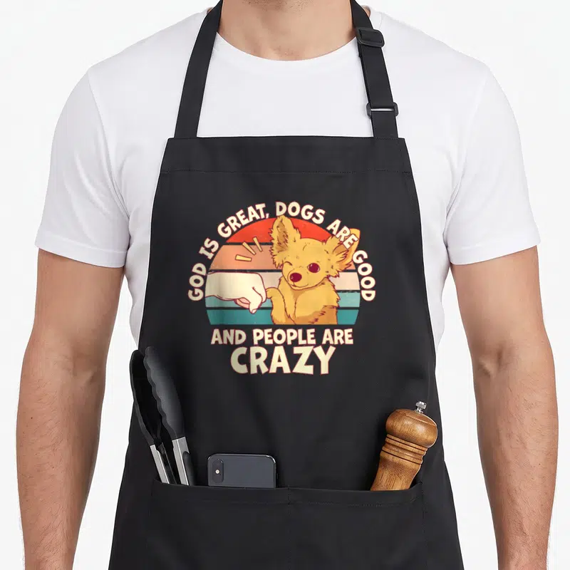 God cooking with dog apron for women - Cartoon dog fist-bumping a hand under retro striped sun with arched text — shown on a black cotton canvas apron against a white background