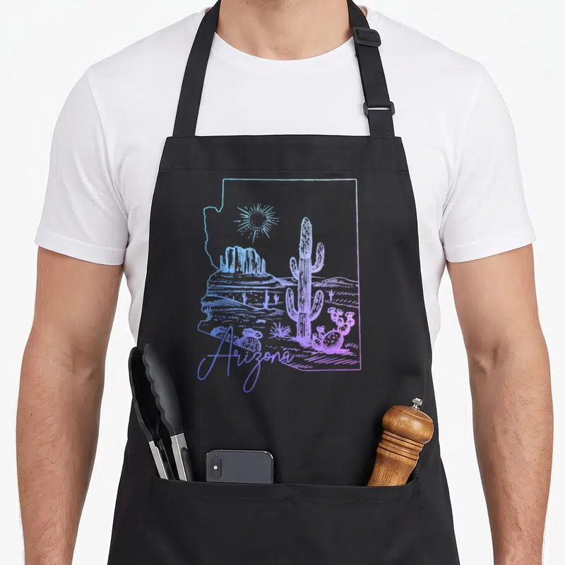 Arizona state cactus apron - Line art saguaro and mesa inside Arizona state outline in blue and purple — shown on a black cotton canvas apron against a white background