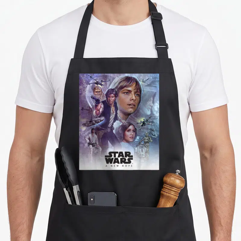 Celebration new hope apron - Star Wars A New Hope montage with Luke Skywalker and two front pockets — shown on a black cotton canvas apron against a white background