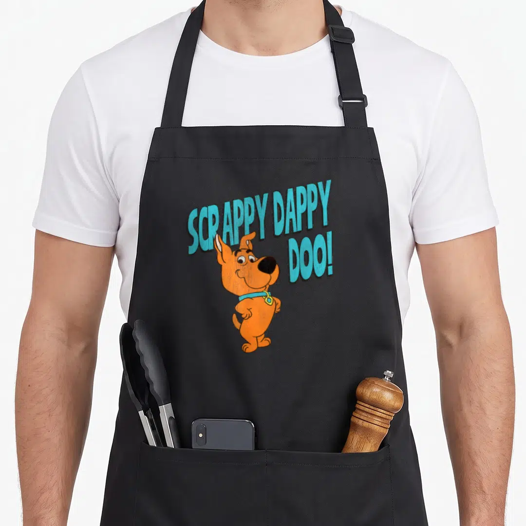 Scrappy popfunk apron - Orange cartoon dog with light blue 'SCRAPPY DAPPY DOO!' text in split layout — shown on a black cotton canvas apron against a white background