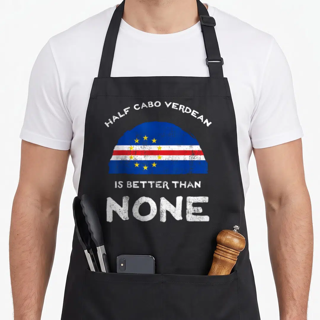 Cape heritage aprons - Distressed half-circle Cabo Verde flag with white text reading HALF CABO VERDEAN IS BETTER THAN — shown on a black cotton canvas apron against a white background