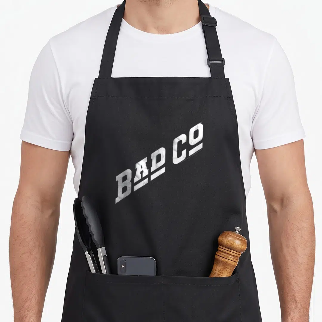 Cute novelty apron for grilling - White distressed BAD CO text angled upward, single line typography design — shown on a black cotton canvas apron against a white background