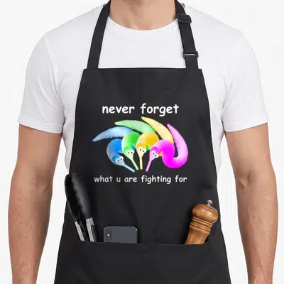 Forget magic apron - Four fuzzy pipe cleaner worms in blue green yellow and pink under white text — shown on a black cotton canvas apron against a white background