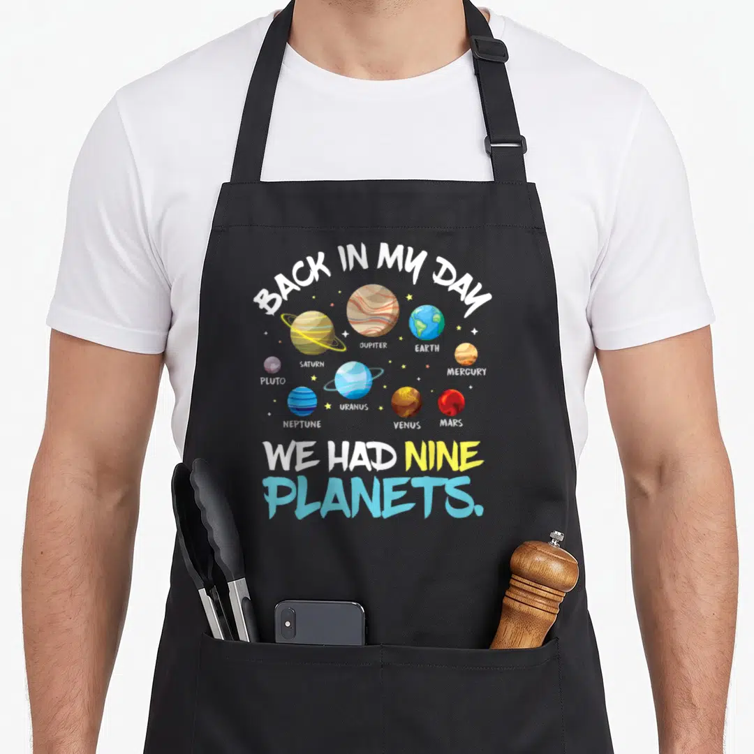 Nine astronaut back apron - Cartoon illustration of nine planets with text Back In My Day We Had Nine Planets — shown on a black cotton canvas apron against a white background