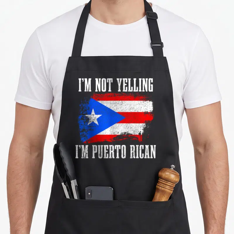 Rico yelling pride apron - Distressed Puerto Rican flag with sarcastic text I'm Not Yelling I'm Puerto Rican in white — shown on a black cotton canvas apron against a white background