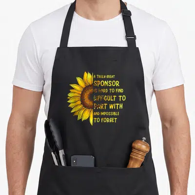 Truly alcohol recovery apron - Sunflower graphic next to sponsor quote text in yellow and orange — shown on a black cotton canvas apron against a white background
