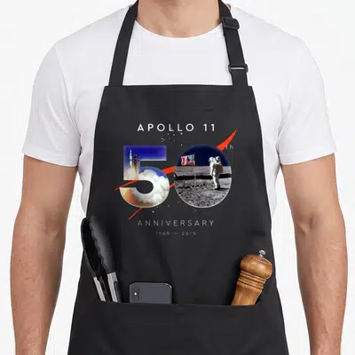 Anniversary apollo apron - Number 50 filled with rocket launch and astronaut photos with red swoosh and anniversary text — shown on a black cotton canvas apron against a white background