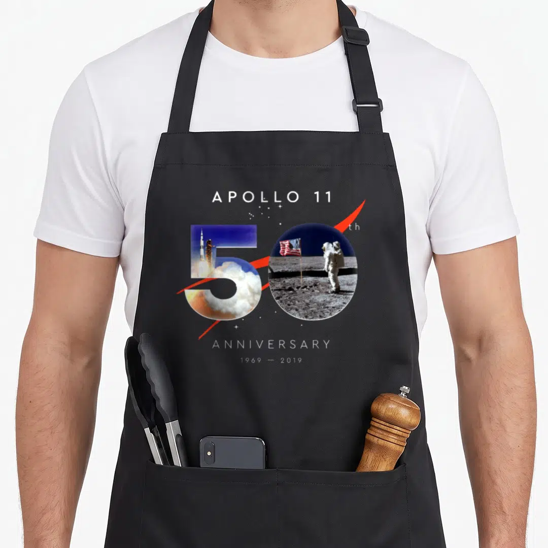 Anniversary apollo apron - Number 50 filled with rocket launch and astronaut photos with red swoosh and anniversary text — shown on a black cotton canvas apron against a white background