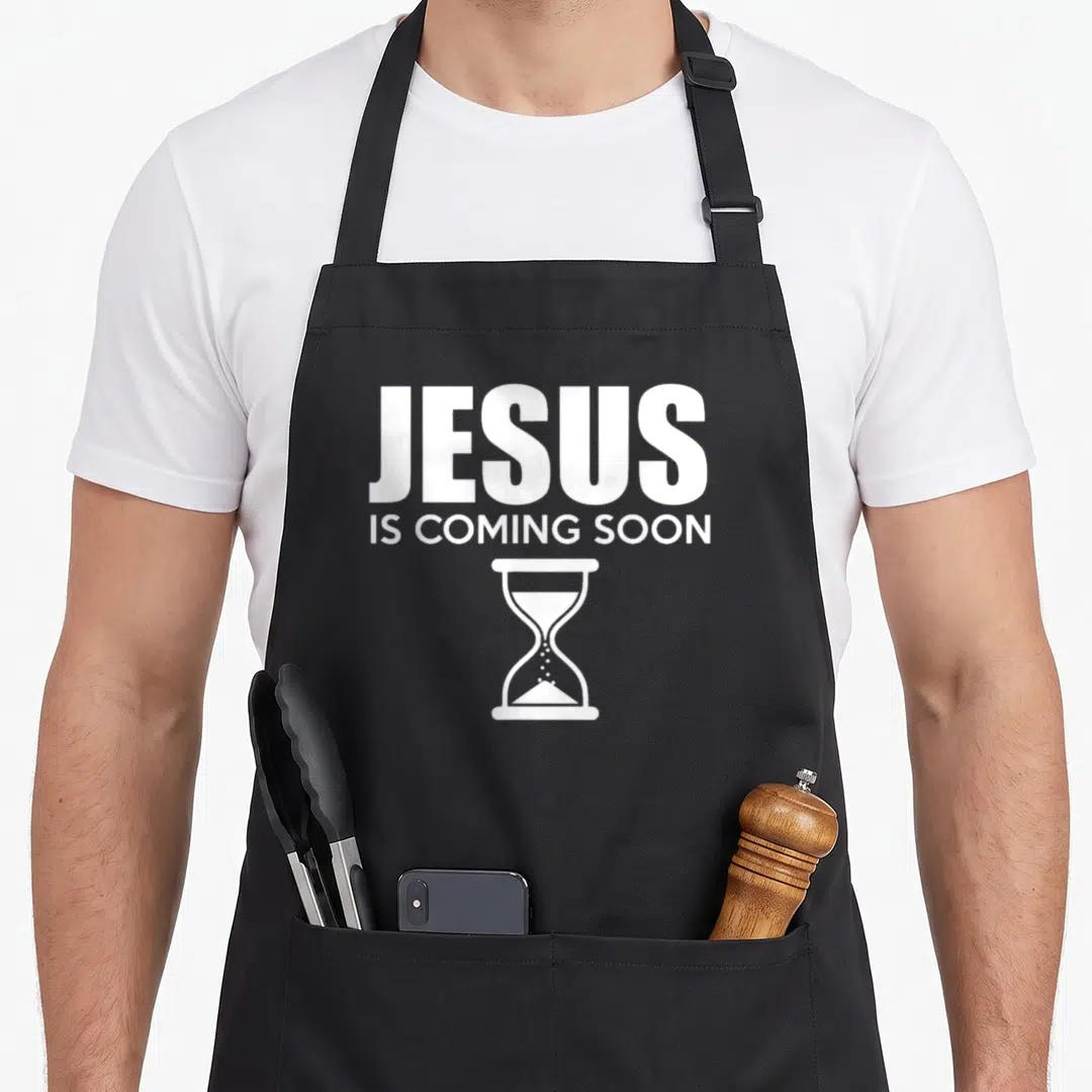 Jesus advent apron - White JESUS IS COMING SOON text above an hourglass icon — shown on a black cotton canvas apron against a white background