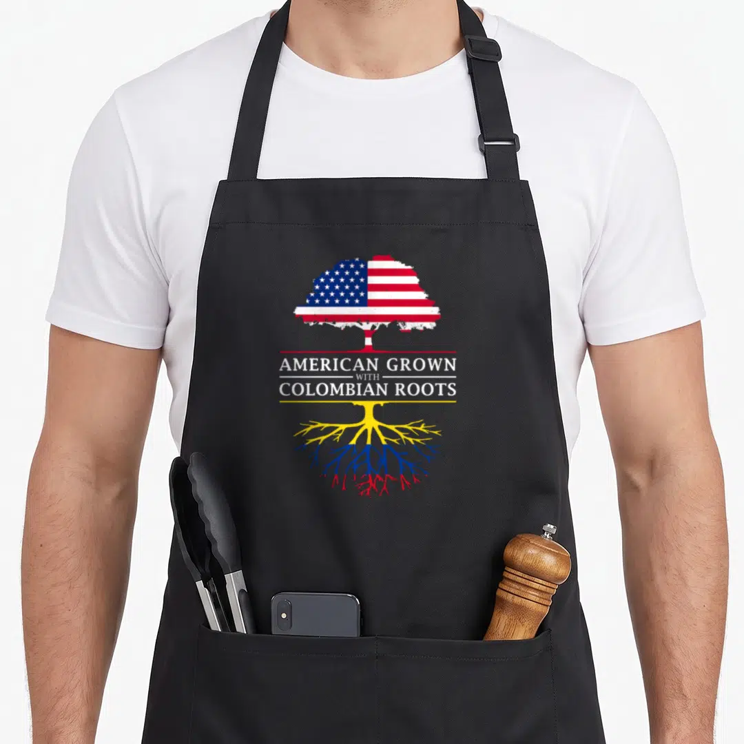 Grown colombian american apron - Tree with US flag canopy and yellow blue red roots separating text AMERICAN GROWN — shown on a black cotton canvas apron against a white background