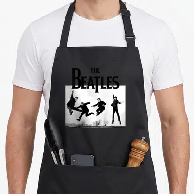 Beatle apron for men - THE Beatles text above photo of four band members jumping in air — shown on a black cotton canvas apron against a white background