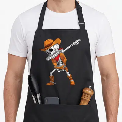 Cowboy halloween apron - Cartoon skeleton dabbing in orange cowboy hat vest and red bandana — shown on a black cotton canvas apron against a white background