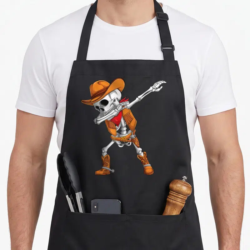 Cowboy halloween apron - Cartoon skeleton dabbing in orange cowboy hat vest and red bandana — shown on a black cotton canvas apron against a white background