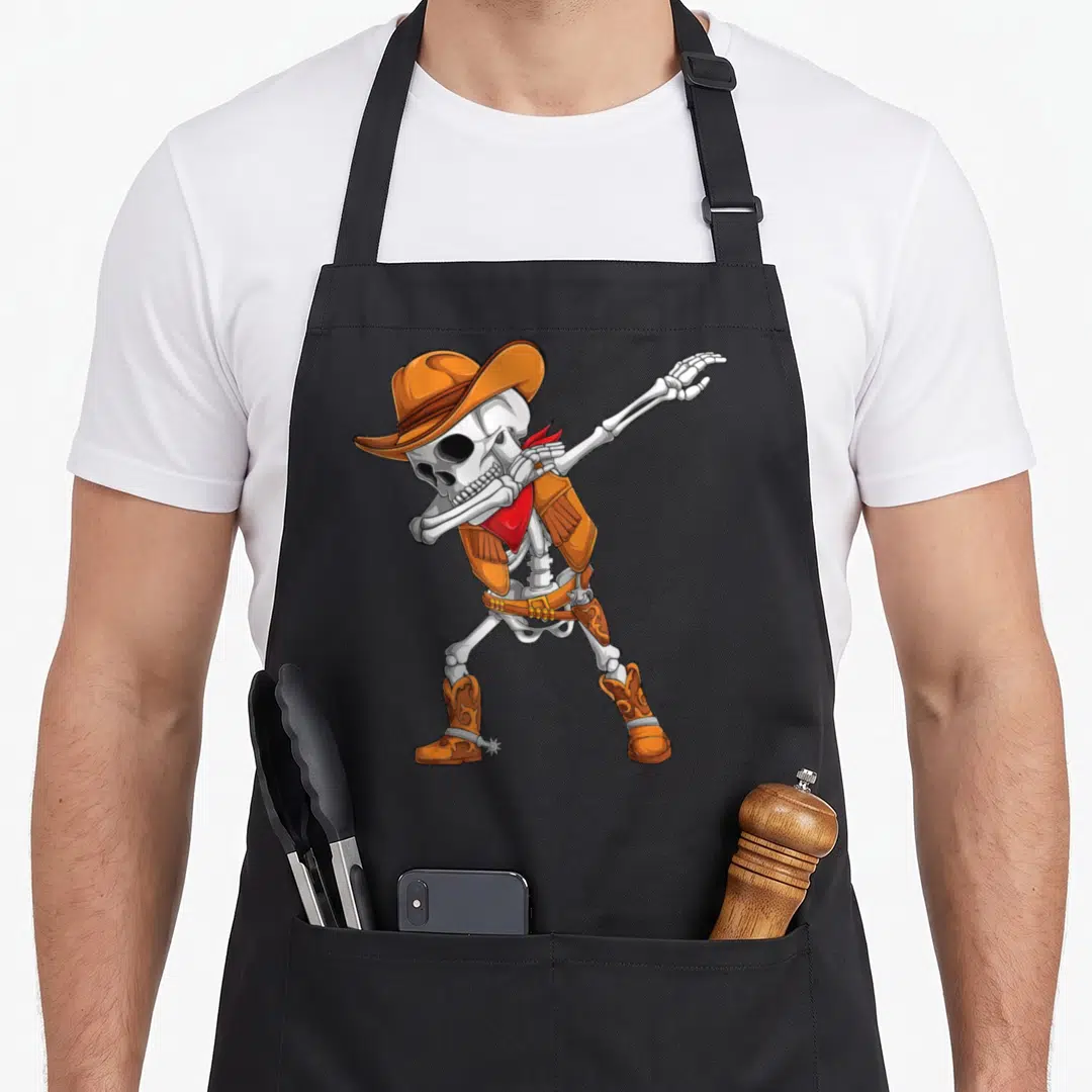 Cowboy halloween apron - Cartoon skeleton dabbing in orange cowboy hat vest and red bandana — shown on a black cotton canvas apron against a white background