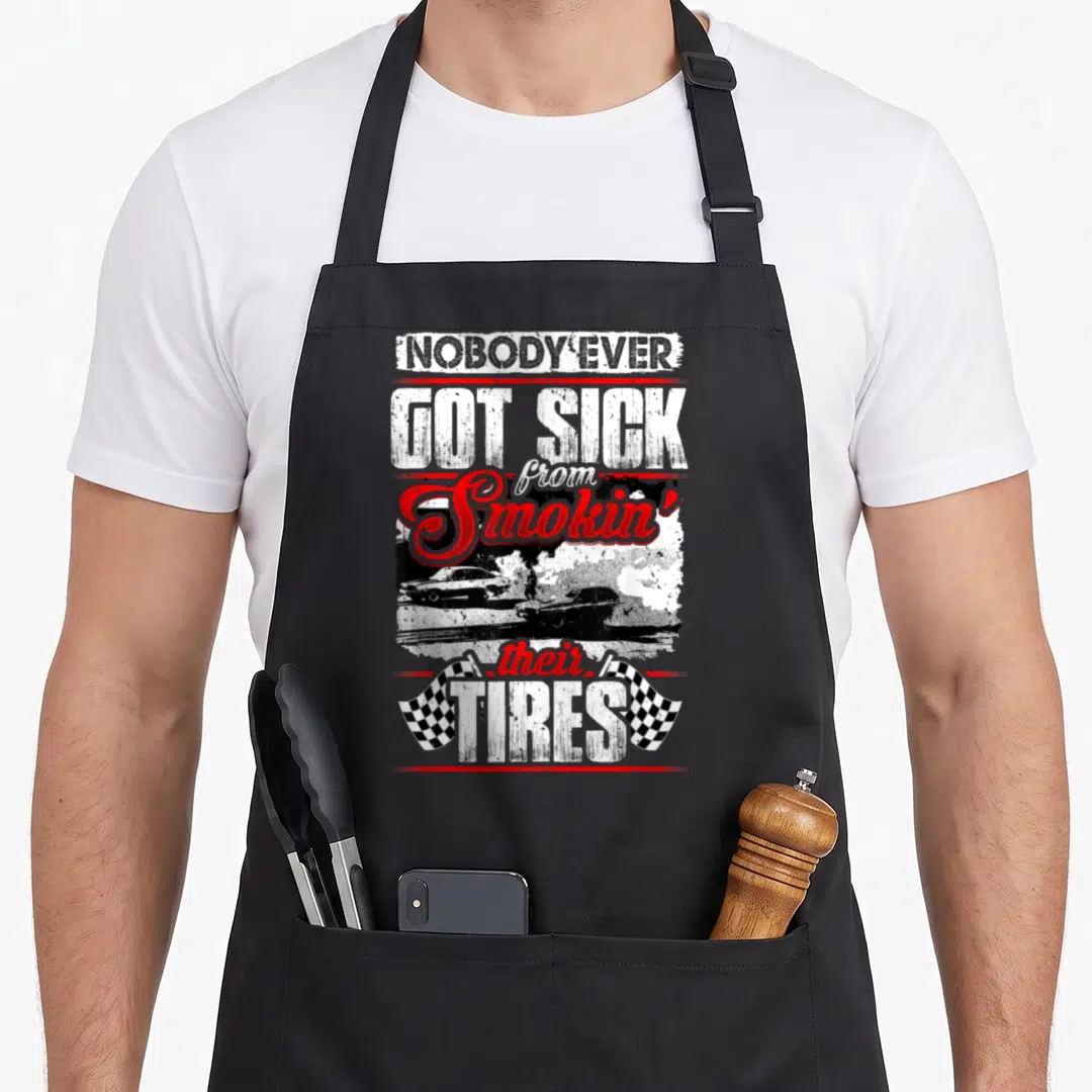 Nobody smoking apron - Stacked text reading nobody ever got sick from smokin their tires above two cars doing a burnout — shown on a black cotton canvas apron against a white background