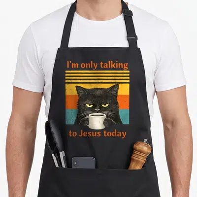 Talking coffee aprons - Black cat holding mug with orange text on retro striped background — shown on a black cotton canvas apron against a white background