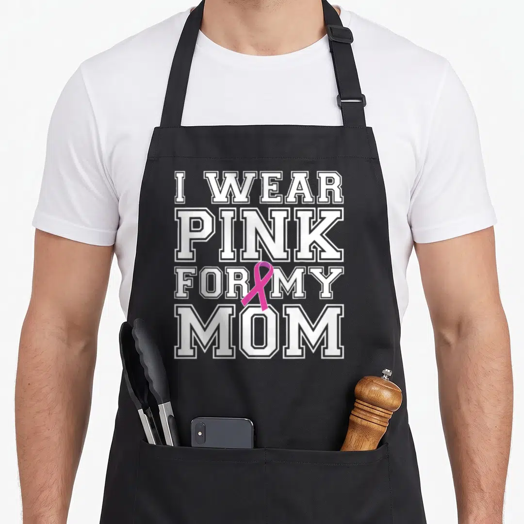 Breast cancer awareness aprons for men - I WEAR PINK FOR MY MOM text with pink ribbon overlapping white letters — shown on a black cotton canvas apron against a white background