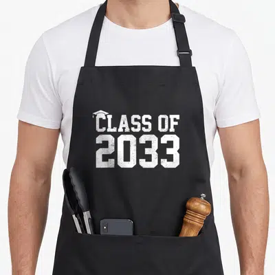 Grow future class apron - White distressed CLASS OF 2033 text with graduation cap icon on black fabric — shown on a black cotton canvas apron against a white background