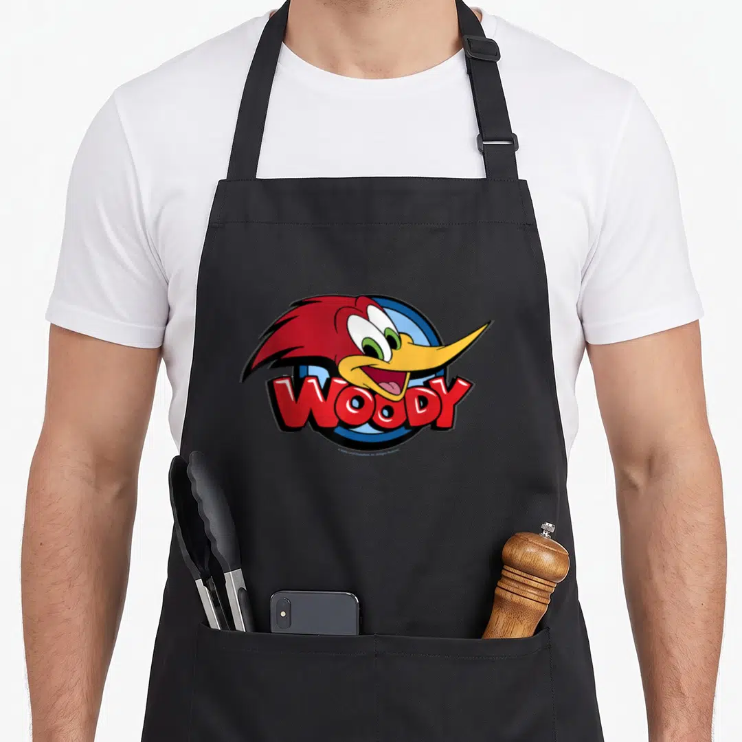 Funny animal face apron - Woody Woodpecker head over blue circle with red WOODY text in cartoon style — shown on a black cotton canvas apron against a white background