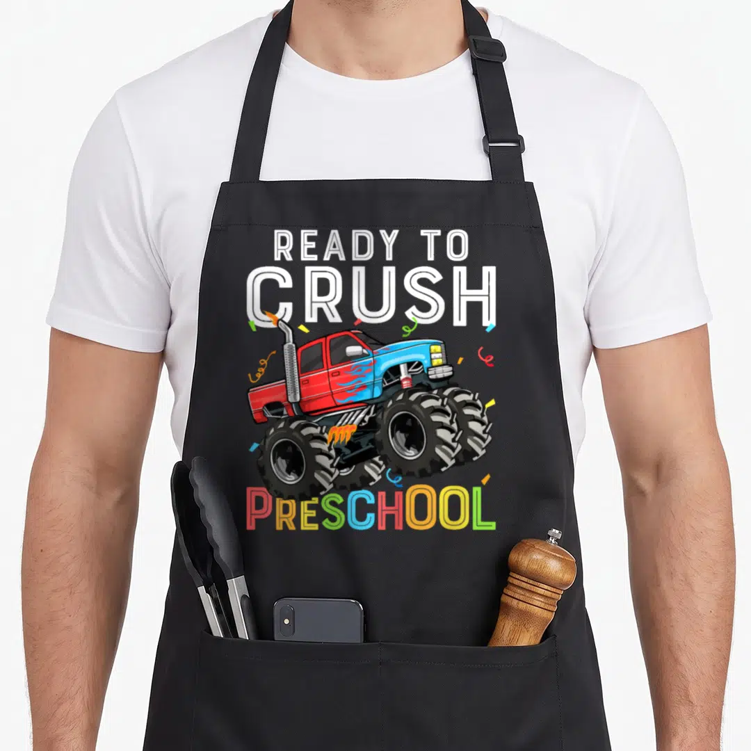 Pre ready truck apron - Monster truck illustration with confetti and colorful PRESCHOOL text — shown on a black cotton canvas apron against a white background
