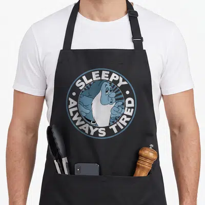 Alway snow white apron - Cartoon dwarf in blue circle with SLEEPY ALWAYS TIRED text — shown on a black cotton canvas apron against a white background