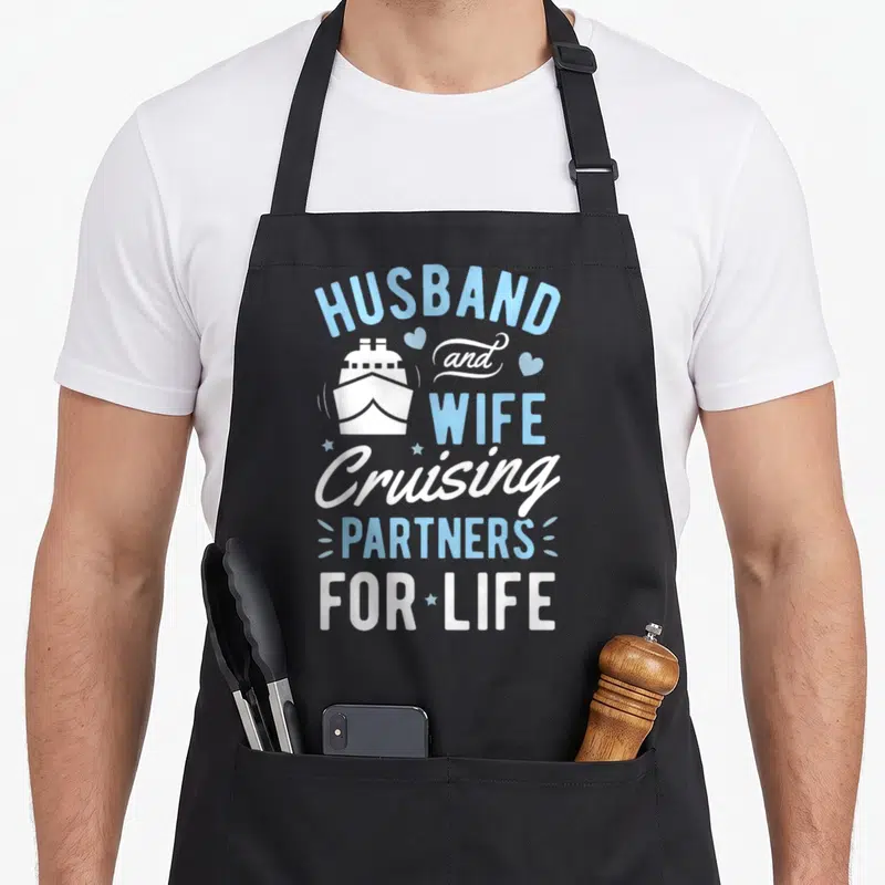 Partner husband wife aprons - Stacked blue and white text reading HUSBAND WIFE Cruising PARTNERS FOR LIFE with cruise — shown on a black cotton canvas apron against a white background