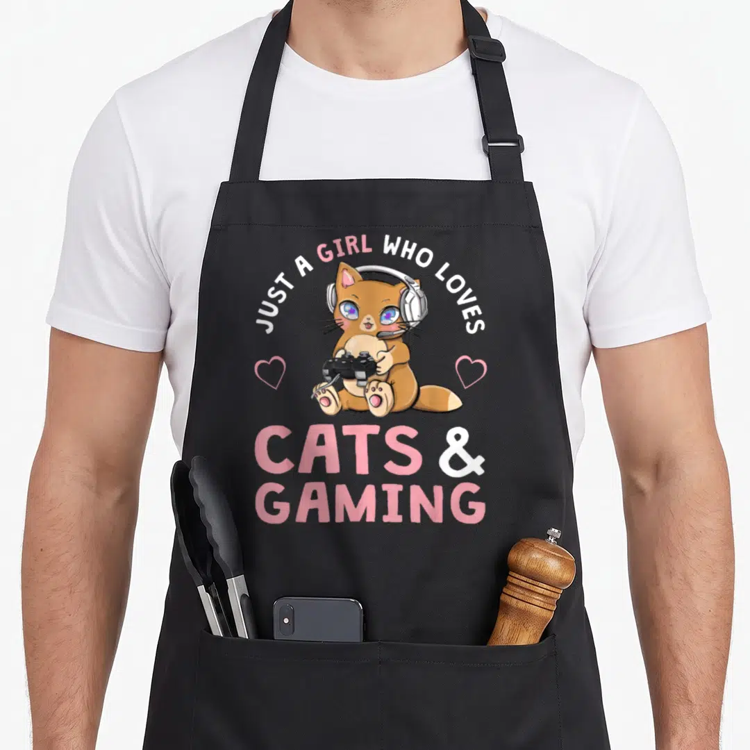 Cat gaming apron - Cartoon brown cat with headset holding controller between two pink hearts under arched text — shown on a black cotton canvas apron against a white background