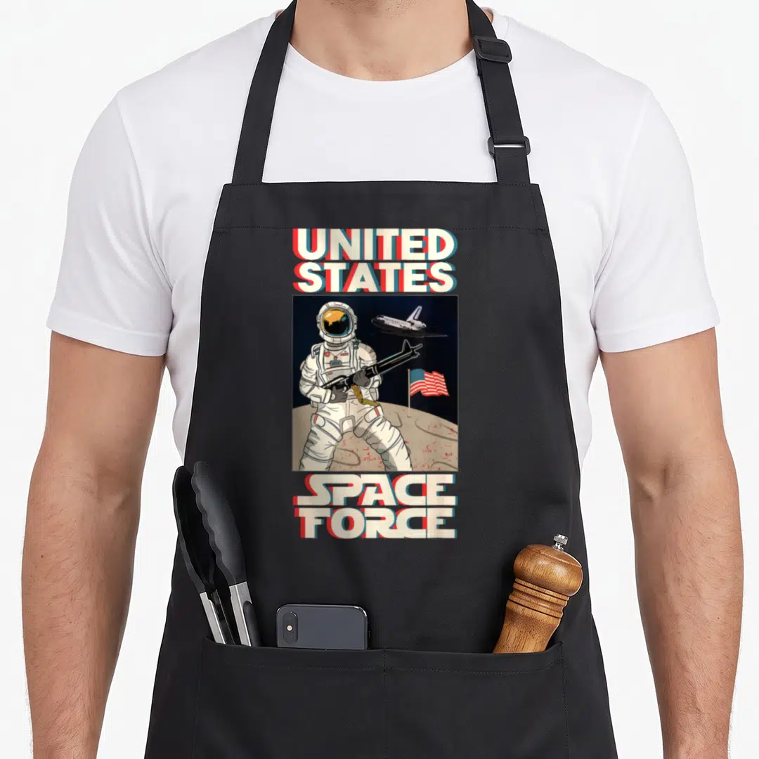 Space badass apron - Retro astronaut with rifle on moon under UNITED STATES SPACE FORCE text — shown on a black cotton canvas apron against a white background