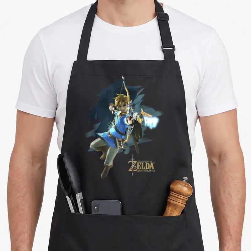 Breath jump apron - Link leaping with bow and shield, gold title text THE LEGEND OF ZELDA BREATH OF THE WILD — shown on a black cotton canvas apron against a white background