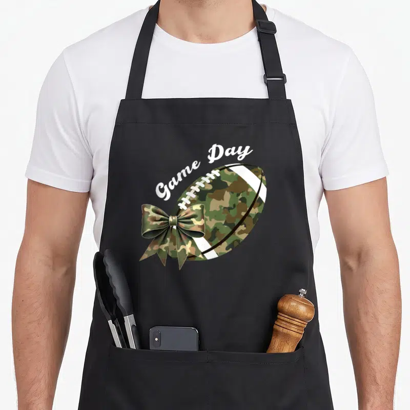 Camouflage camo apron - Camo football with bow and arched Game Day text in white script — shown on a black cotton canvas apron against a white background