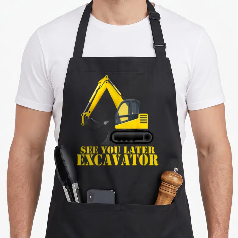 Later excavator girl apron - Yellow cartoon excavator above yellow text reading SEE YOU LATER EXCAVATOR on grey — shown on a black cotton canvas apron against a white background
