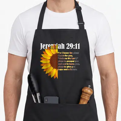 Plan christian apron - Half sunflower next to stacked Jeremiah 29:11 text in orange and brown — shown on a black cotton canvas apron against a white background