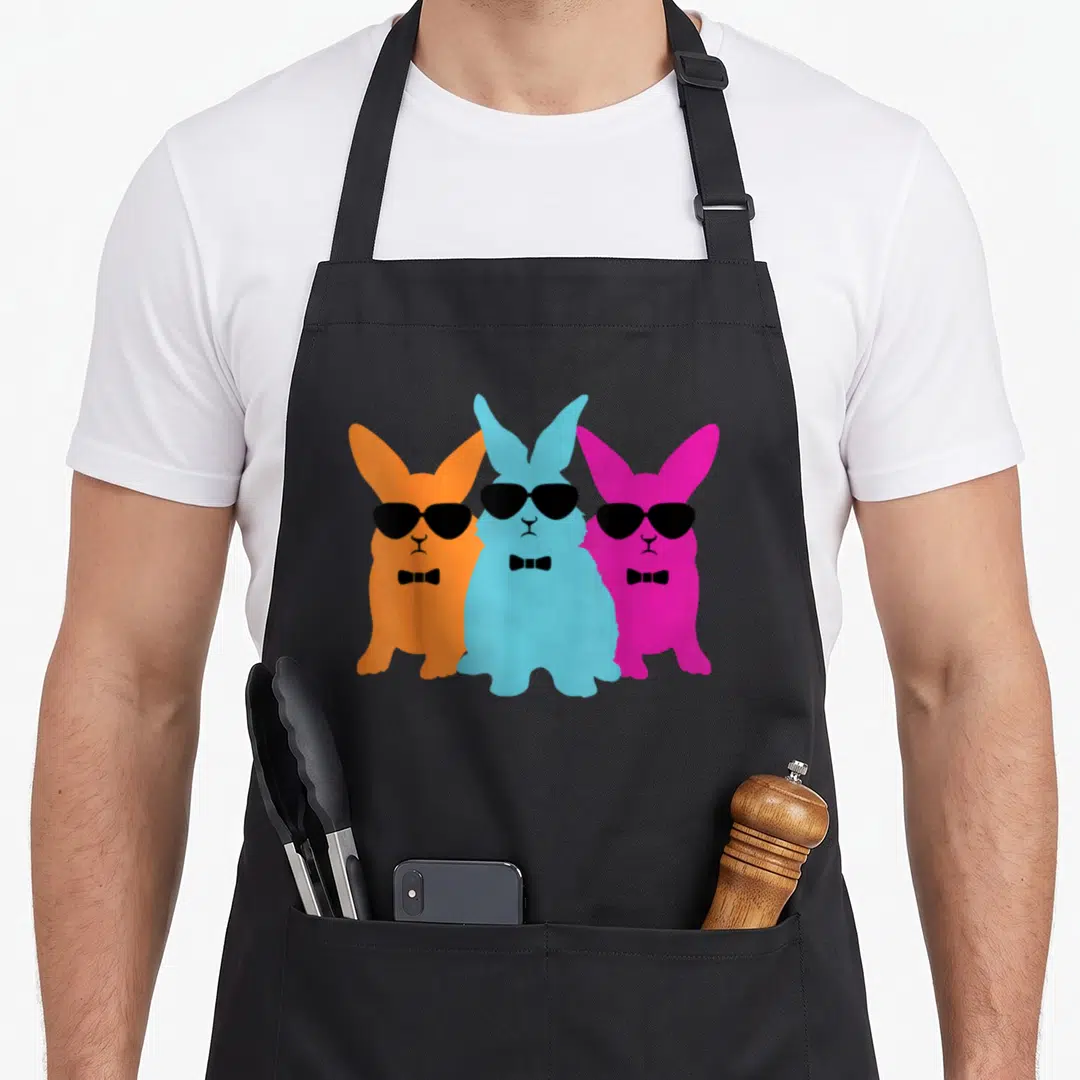 Hipster easter bunny aprons - Three cartoon rabbits in orange, blue, and pink wearing black sunglasses and bow ties — shown on a black cotton canvas apron against a white background