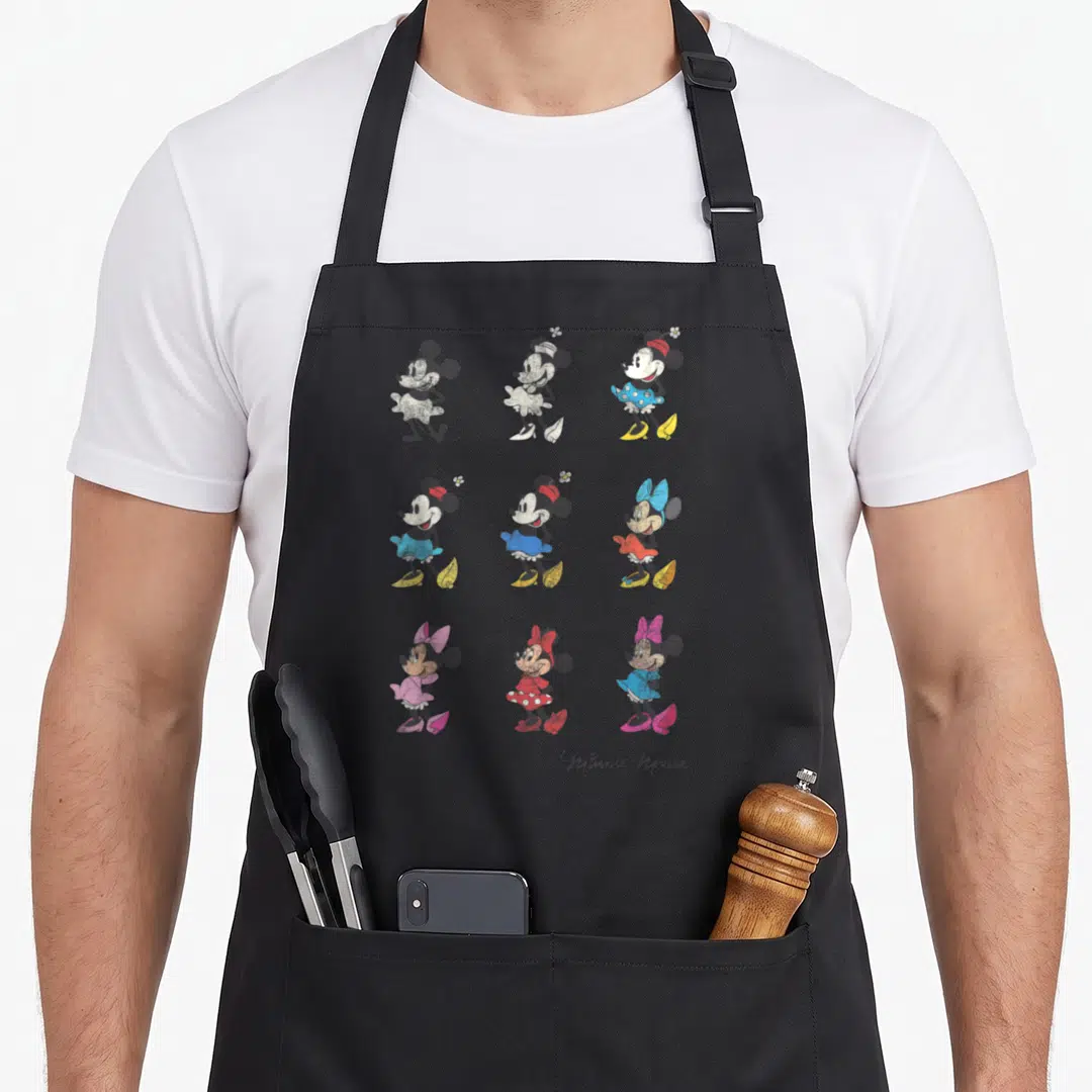 Through friends apron - Nine Minnie Mouse cartoons in a grid with black, white, blue, red, pink, and yellow details — shown on a black cotton canvas apron against a white background