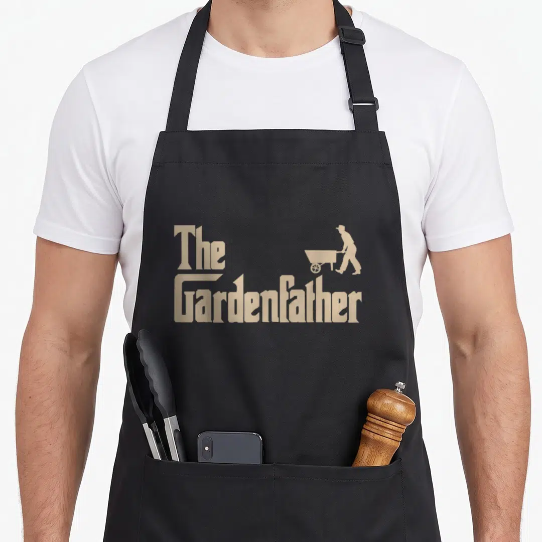 Gardening shrub apron - Tan text The Gardenfather with man pushing wheelbarrow silhouette — shown on a black cotton canvas apron against a white background