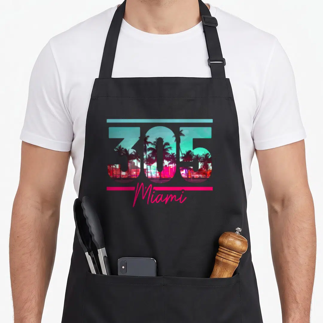 Miami area tree apron - 305 number containing palm tree and building scene with Miami script below — shown on a black cotton canvas apron against a white background